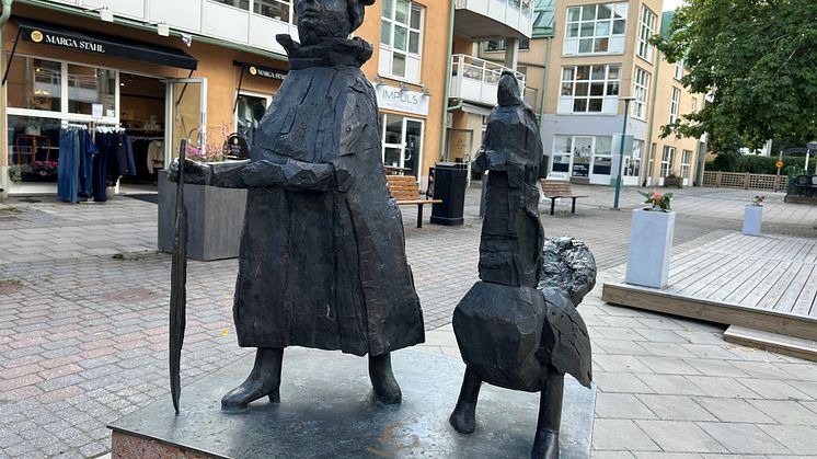 Skulptur av en kvinna som går bredvid en tjäder, i handen håller hon en fjäder. 