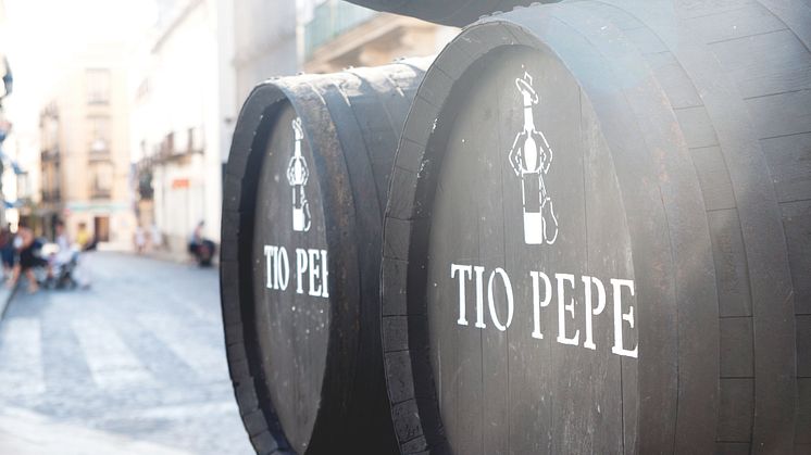 Kaksi suurta puista Tio Pepe -tynnyriä kivikadulla perinteisessä kaupunkiympäristössä, taustalla rakennuksia ja ihmisiä