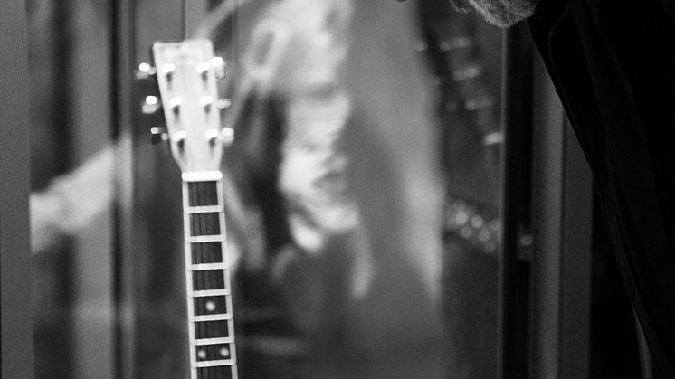 Person bøyer seg og ser på gitar. Foto.
