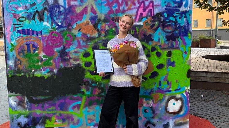 Dansstipendiat My Primbom med diplom och blombukett framför graffitivägg vid Kulturkvarteret