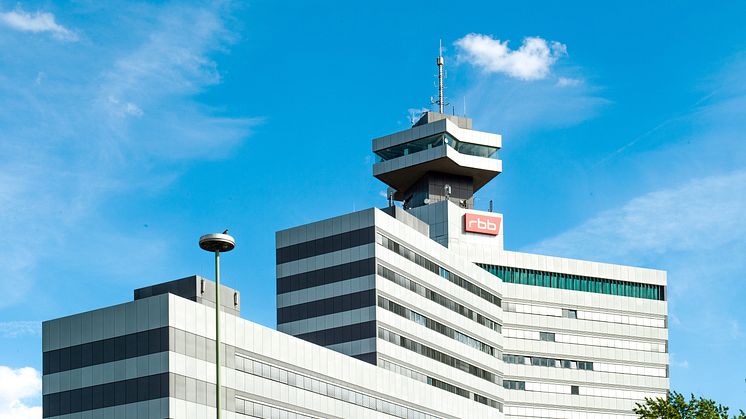 Modernes Bürogebäude mit rbb-Logo und markantem Sendeturm vor blauem Himmel.