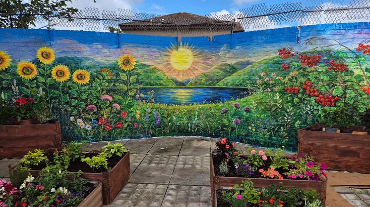 A colourful mural showing green hills and a sunset with garden planter boxes in front