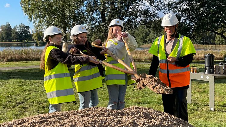 Tre barn gräver i en sandhög med en spade med tre handtag. 