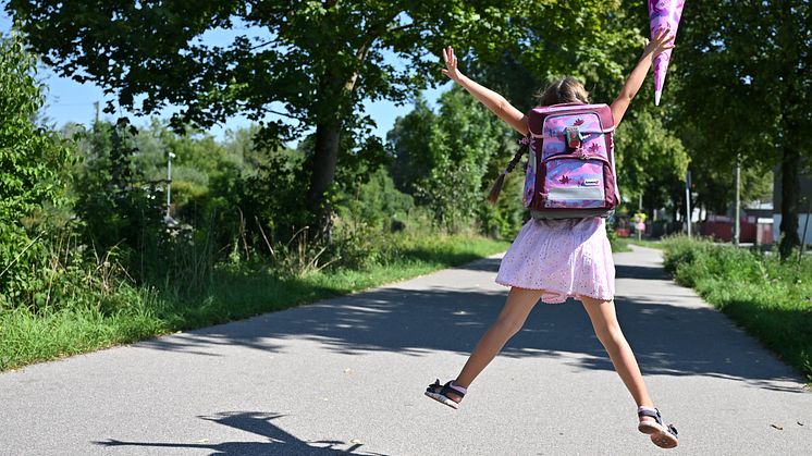 Mädchen mit Schulranzen und Schultüte freut sich und springt in die Luft.