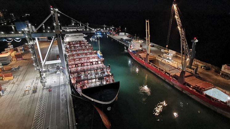 Fartyg förtöjt vid kaj i containerterminal, med belysning från fartyg och hamnutrustning.