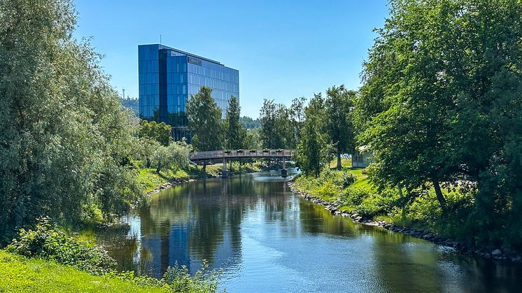En kanal och lummig grönska i förgrunden. I fonden ett hotell med flera våningar.
