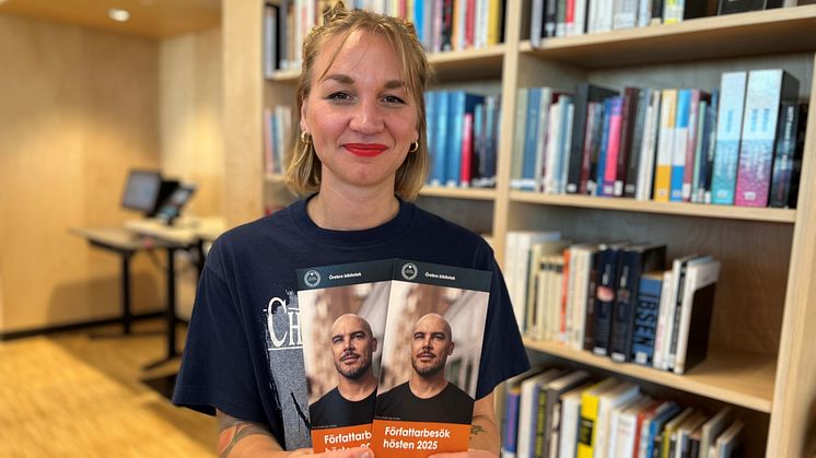 Kvinna visar upp programblad för Författarbesök hösten 2025 i biblioteket