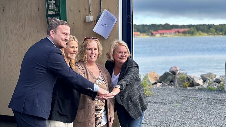 Tre kvinnor och en man skakar hand stående i öppningen till en container framför havet