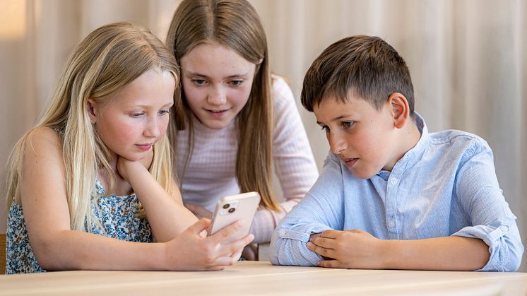 Tre børn ser på en smartphone sammen