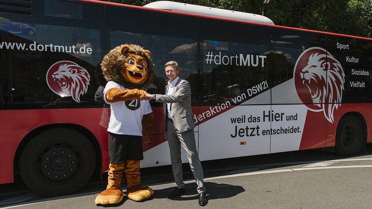 Maskottchen KIM und Vorstandsvorsitzender vor einem Bus
