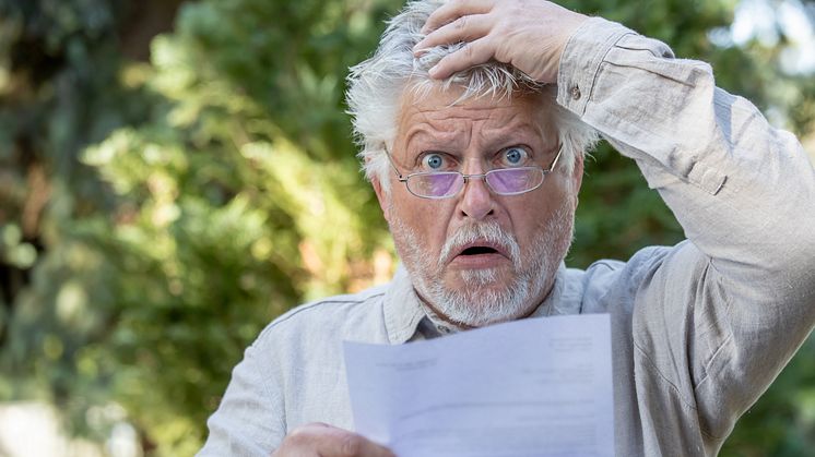 Älterer Mann mit Brille blickt erschrocken auf ein Schreiben und fasst sich mit der Hand an den Kopf.