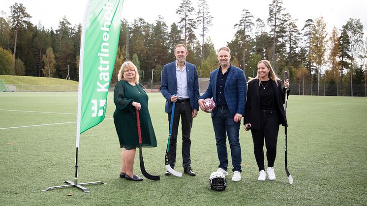 Fyra personer står med idrottsutrustning på en fotbollsplan.