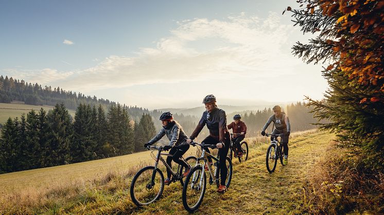 zu sehen ist eine Familie auf Fahrrädern, die durch eine bunte Herbstlandschaft fahren