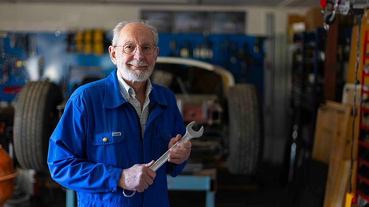 En man i blå arbetskläder med en skiftnyckel i sin hand står i ett garage