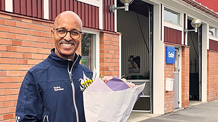 Leende man med blombukett utanför en tegelbyggnad.