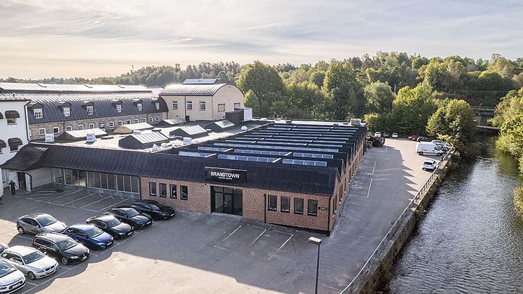 Övrsiktsbild på fastigheten Forsen i Borås, intill ån Viskan i fint sensommarväder, med en återställd rödbrun tegelfasad.