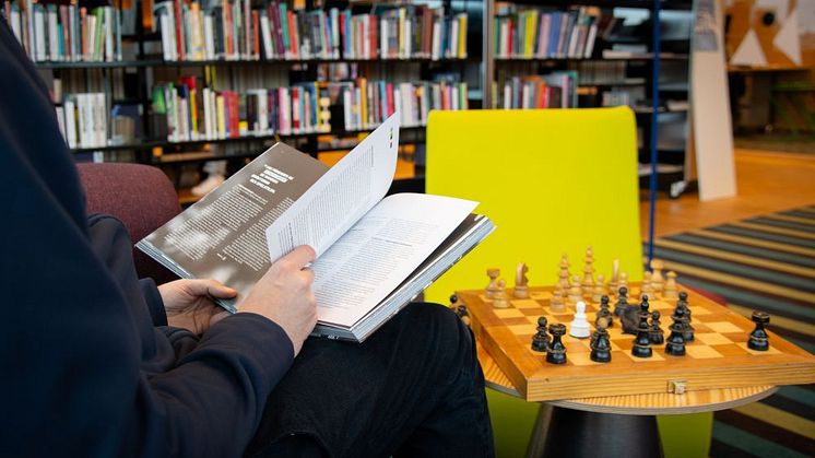 En person sitter och bläddrar i en bok på ett bibliotek. 