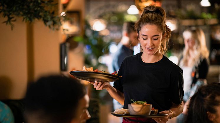 Kvinnlig servitris bär två tallrikar med mat i en restauranglokal.