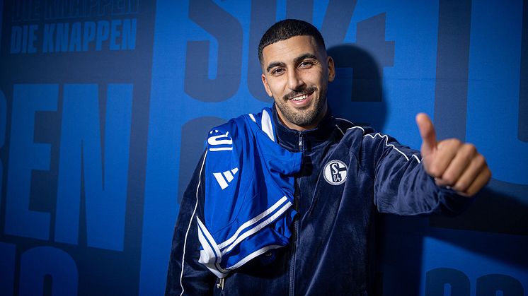 Aymen Barkok steht vor Schalke-Wand und zeigt mit dem Daumen nach oben