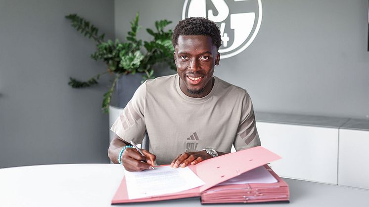 Christian Gomis unterschrieb einen langfristigen Vertrag, ist hier mit Stift und Unterschriftenmappe zu sehen.