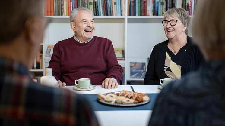 Fyra personer sitter vid ett bord dukat med ett bullfat. En herre och en dam skrattar, ryggarna av två personer som också.