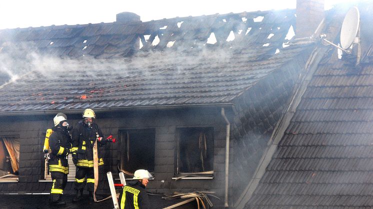 Räddningstjänst släcker en omfattande vindsbrand i ett flerbostadshus med skador på taket.