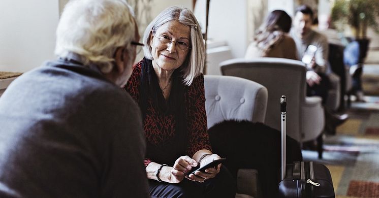 Två pensionärer sitter och pratar med varandra i en hotell lobby.
