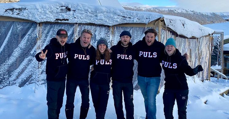 Sex medarbetare från Puls står tillsammans utomhus i snölandskap i Vemdalen, iklädda svarta tröjor mvinterlandskap i Vemdalen