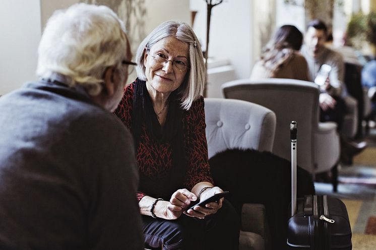 Två pensionärer sitter och pratar med varandra i en hotell lobby.