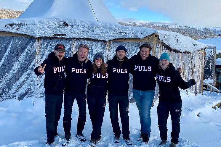 Sex medarbetare från Puls står tillsammans utomhus i snölandskap i Vemdalen, iklädda svarta tröjor mvinterlandskap i Vemdalen