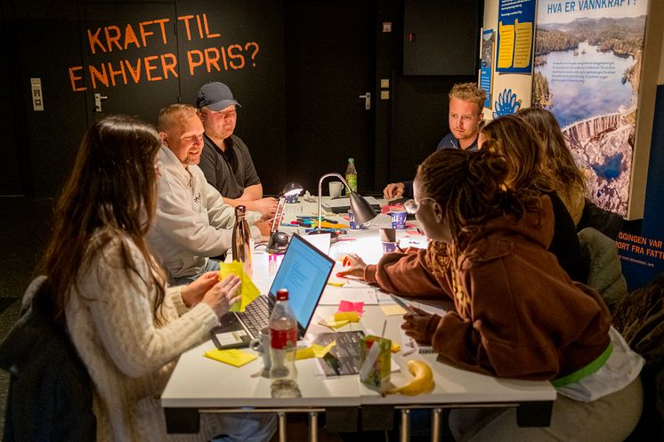 7 engasjerte deltagere rundt et bord med pc'er og gule lapper på bordet