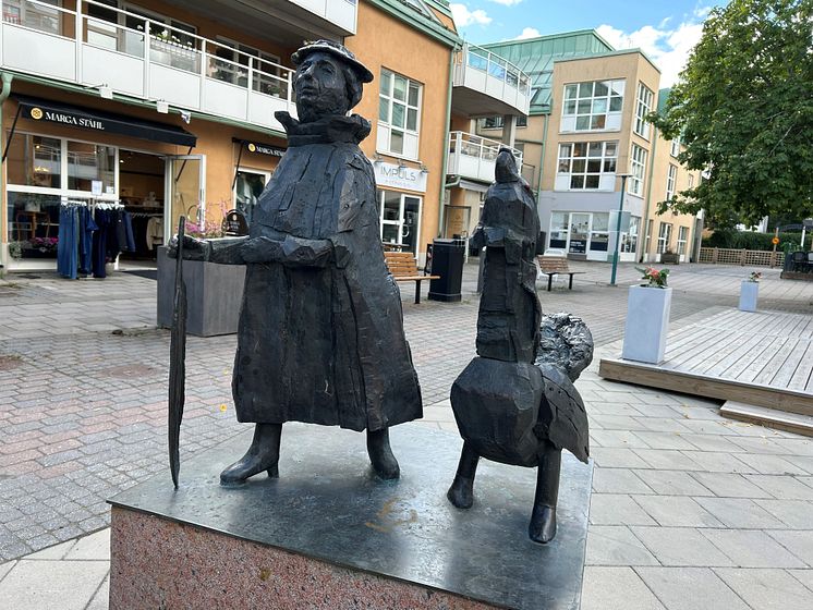 Skulptur av en kvinna som går bredvid en tjäder, i handen håller hon en fjäder. 