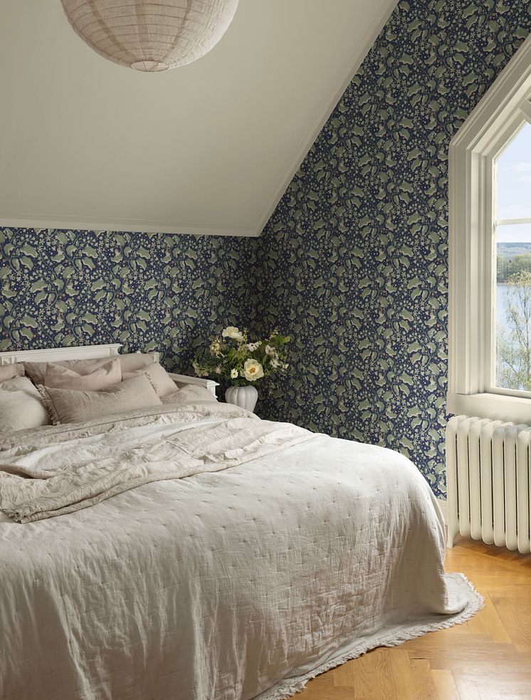 Tapet med mörkblå botten och blad och blommor i grönt och terrakotta i mysigt sovrum.