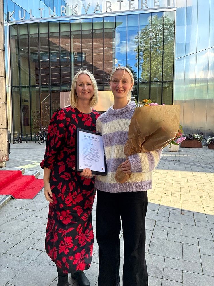 Två kvinnor med diplom och blombukett framför Kulturkvarteret i Örebro