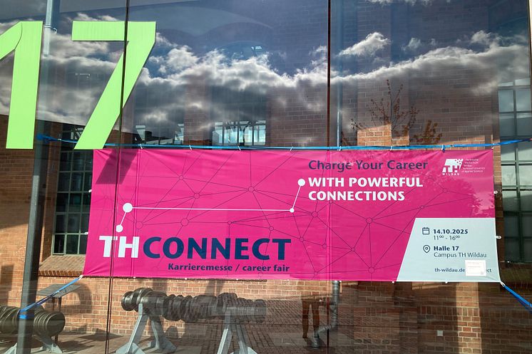 Pinkfarbenes Banner mit der Aufschrift THCONNECT hängt in der Glasfront von Halle 17 auf dem Campus der TH Wildau.
