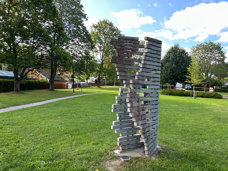 Betongelement är staplade på varandra som en öppen bok, skulpturen står i en grönskande park. 