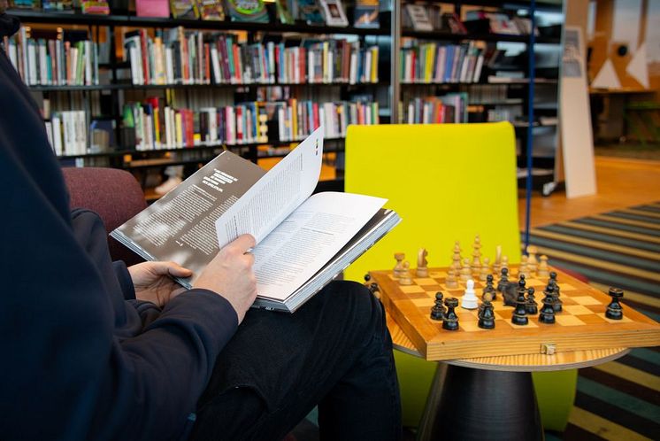 En person sitter och bläddrar i en bok på ett bibliotek. 