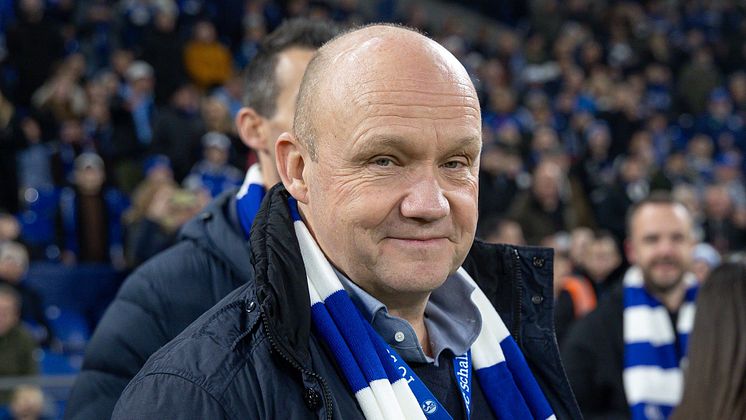 Franz Lotze lächelt in die Kamera mit Schalke-Fans im Hintergrund